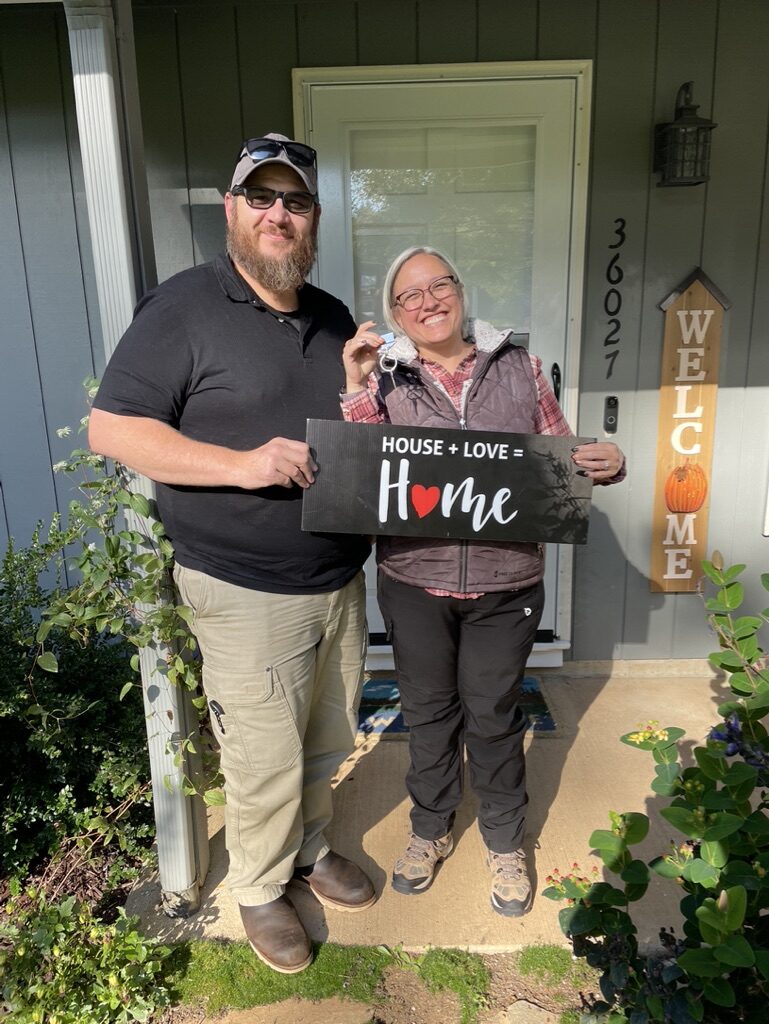 Robin and Jeromy holding a House + Love = Home sign at their new farmhouse